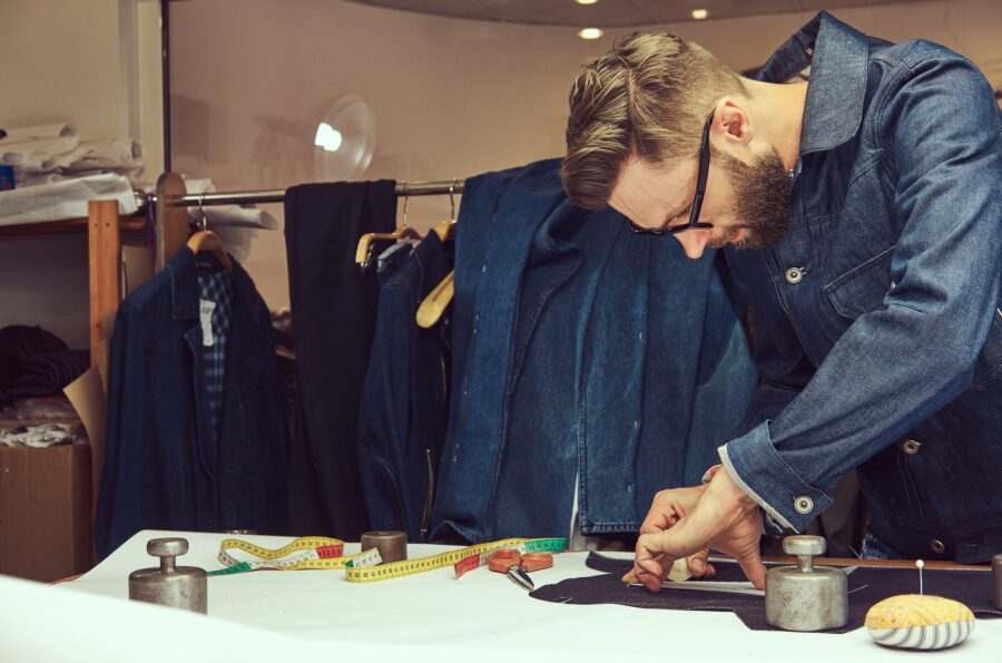 handsome-bearded-tailor-working-with-cloth-samples-sewing-workshop-min handsome-bearded-tailor-working-with-cloth-samples-sewing-workshop-min